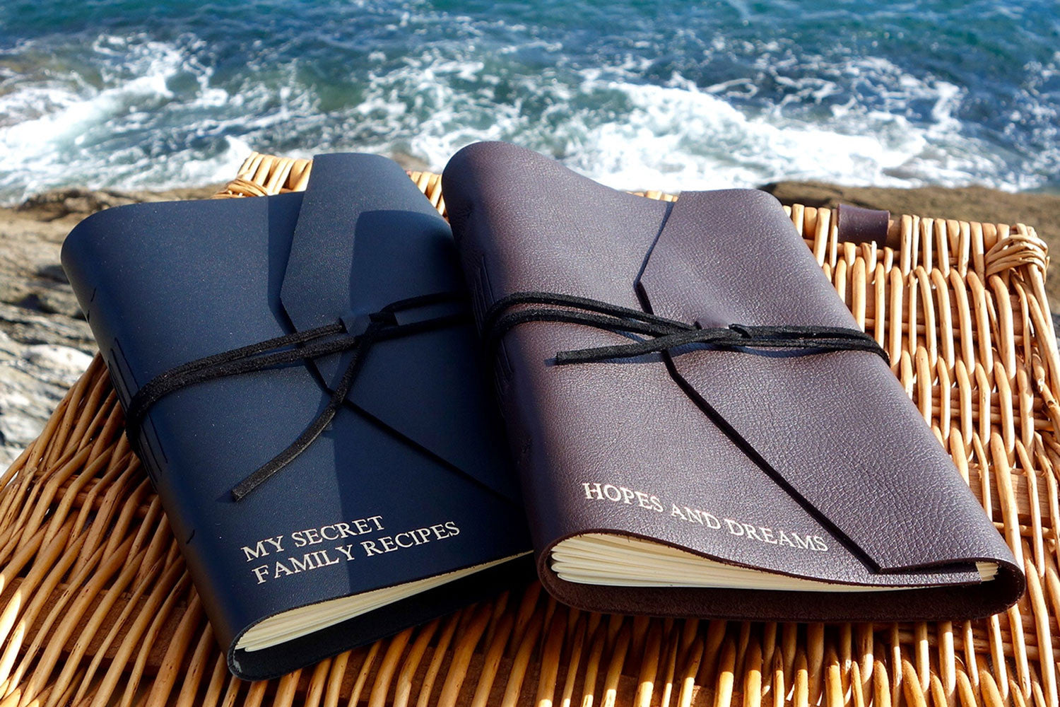 Two leather journals on a picnic hamper by the sea, personalised with My secret family recipes and Hopes and dreams