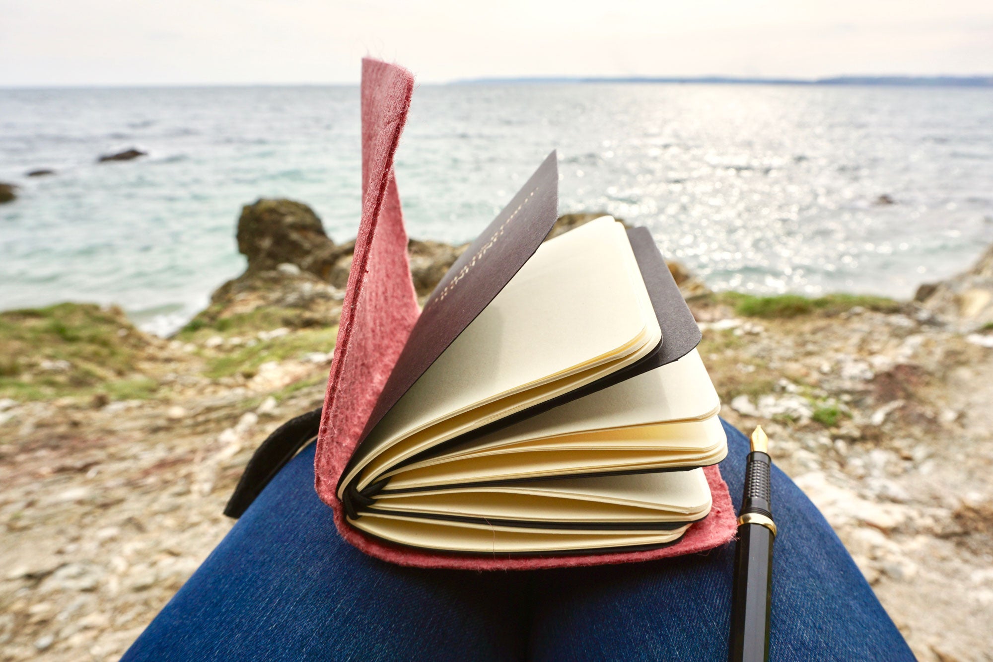 what3words Vegan Leather Journal in Pink pineapple leather shown here in use on someones lap whilst looking out to sea